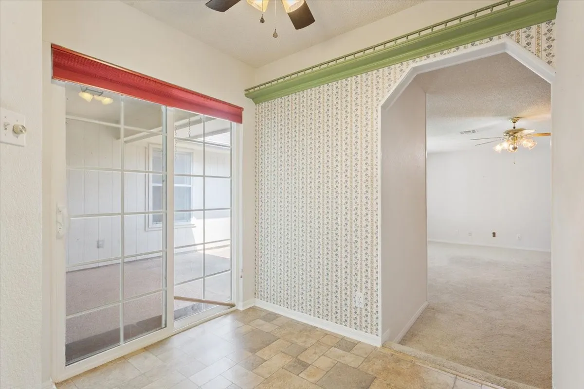Spare room featuring ceiling fan, light colored carpet, a textured ceiling, light stone finish flooring, and arched walkways