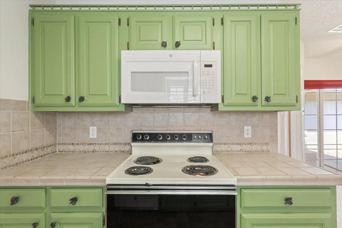 Kitchen with green cabinetry, white appliances, backsplash, a textured ceiling, and tile counters