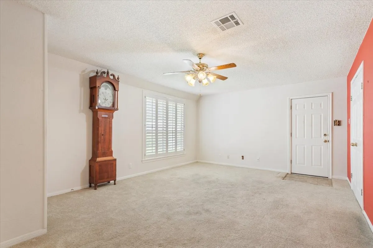 Empty room featuring light colored carpet, a textured ceiling, and a ceiling fan