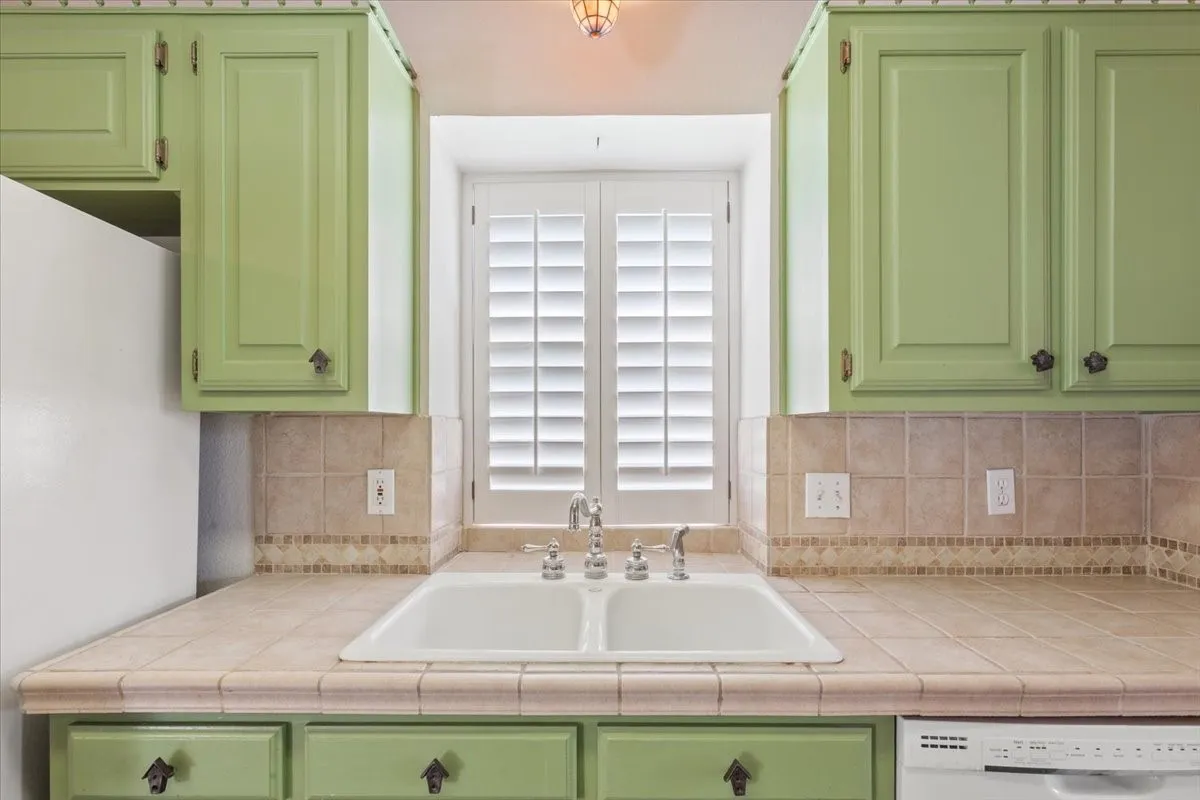 Kitchen with green cabinets, white appliances, and backsplash