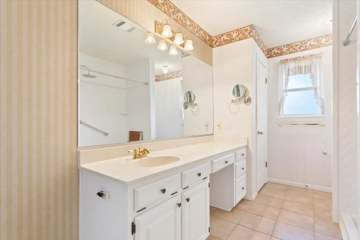 Full bathroom featuring vanity, light tile patterned floors, a shower, wallpapered walls, and a textured ceiling