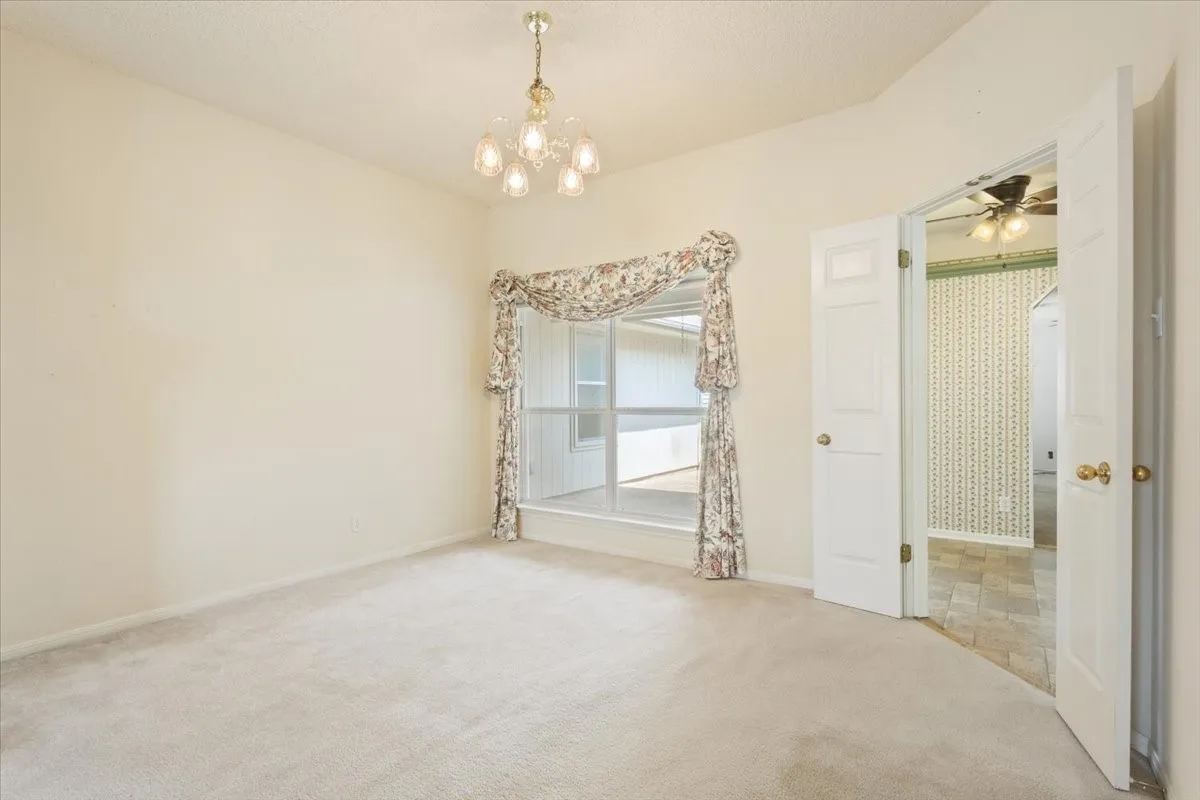 Carpeted empty room featuring a chandelier and ceiling fan