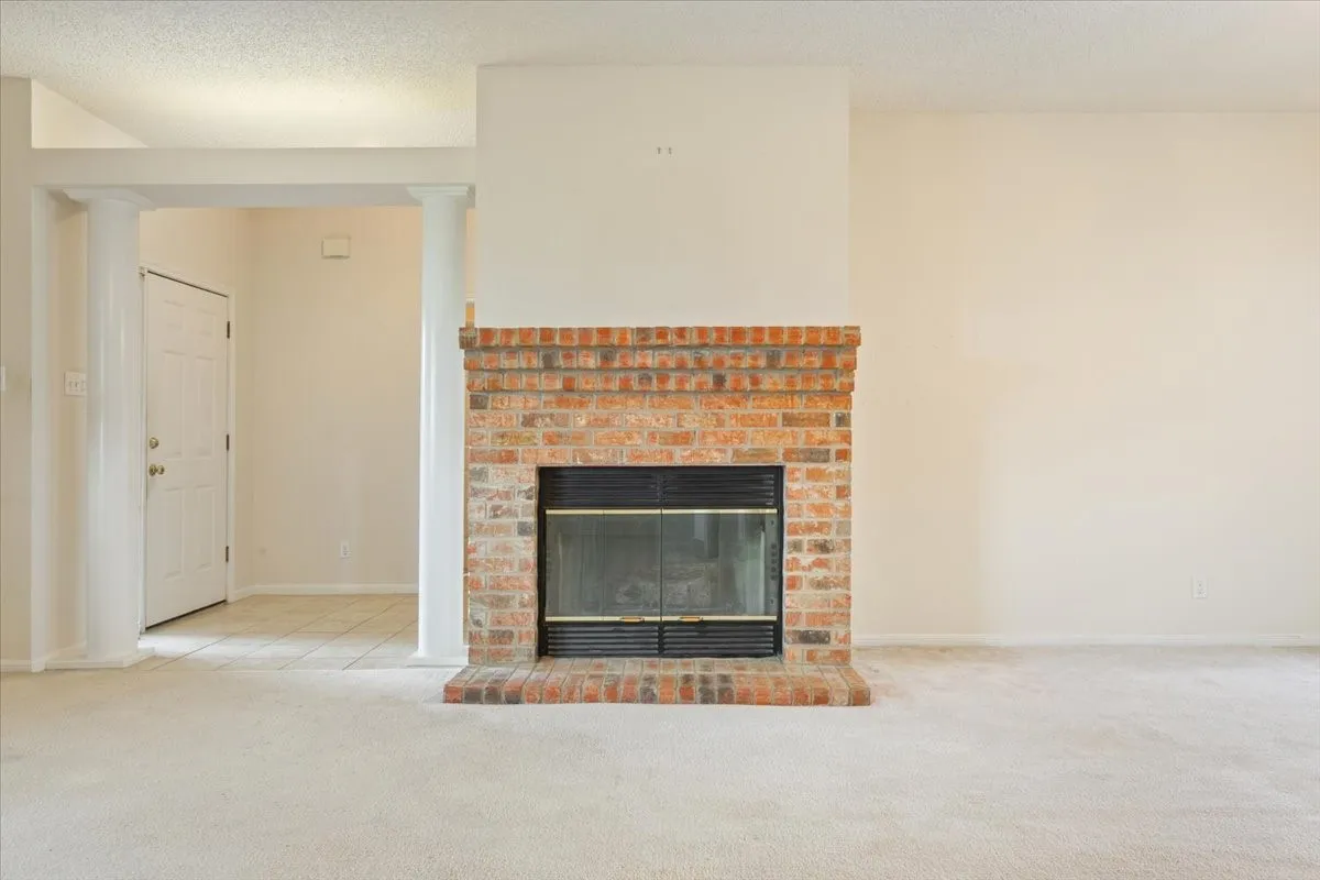 Unfurnished living room featuring carpet, a fireplace, a textured ceiling, and ornate columns