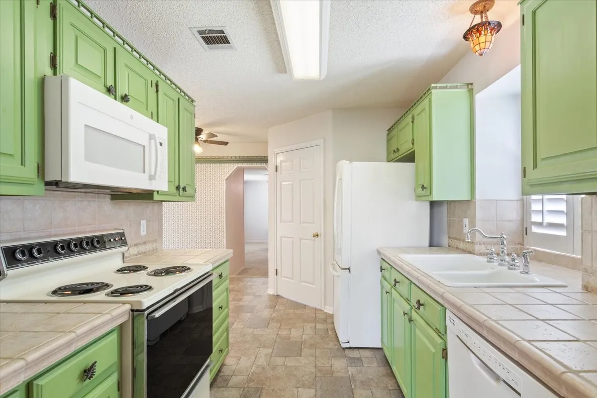 Kitchen featuring green cabinets, white appliances, backsplash, a textured ceiling, and stone finish flooring