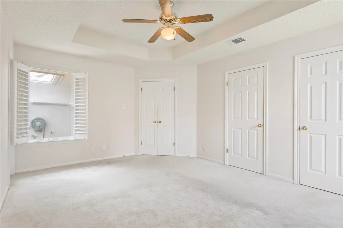 Unfurnished bedroom with a raised ceiling, carpet flooring, a ceiling fan, two closets, and a textured ceiling