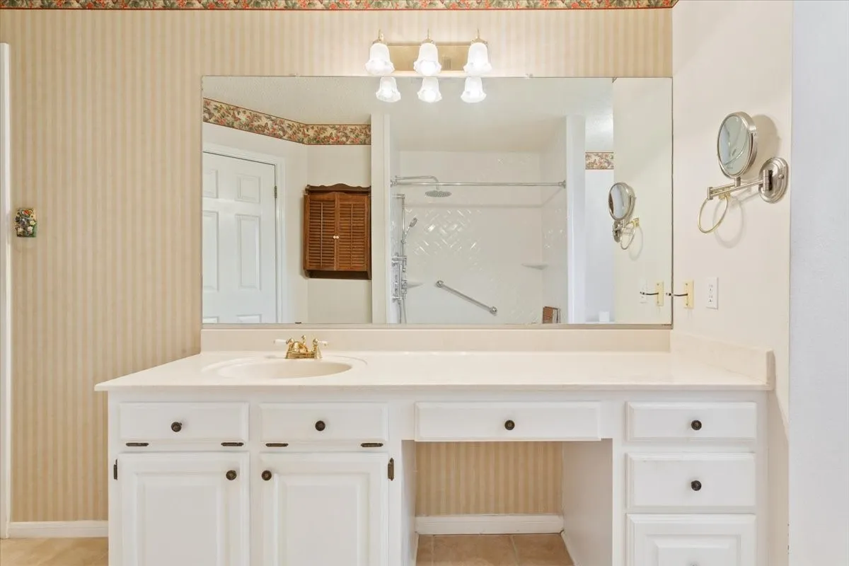 Full bath with a shower stall, wallpapered walls, vanity, and light tile patterned flooring