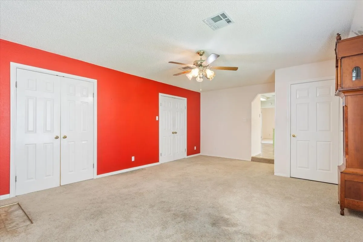 Unfurnished bedroom featuring light colored carpet, a ceiling fan, two closets, and a textured ceiling