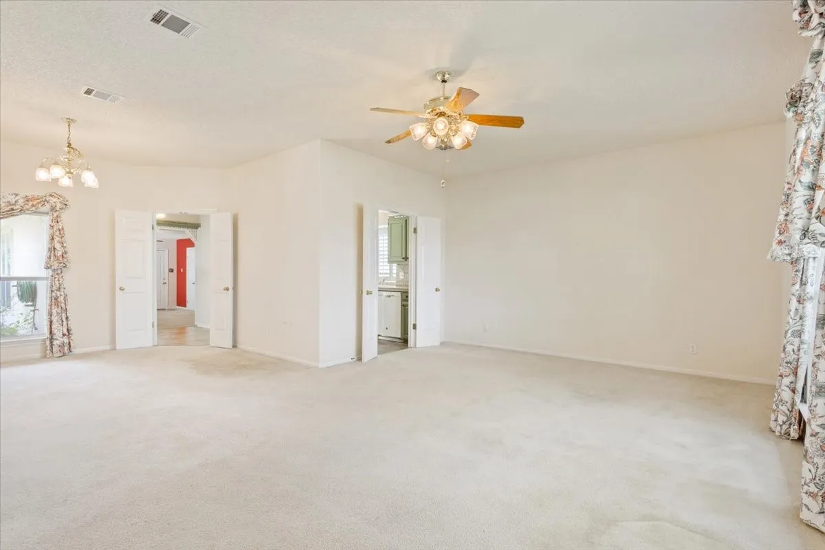 Carpeted empty room featuring ceiling fan and a chandelier