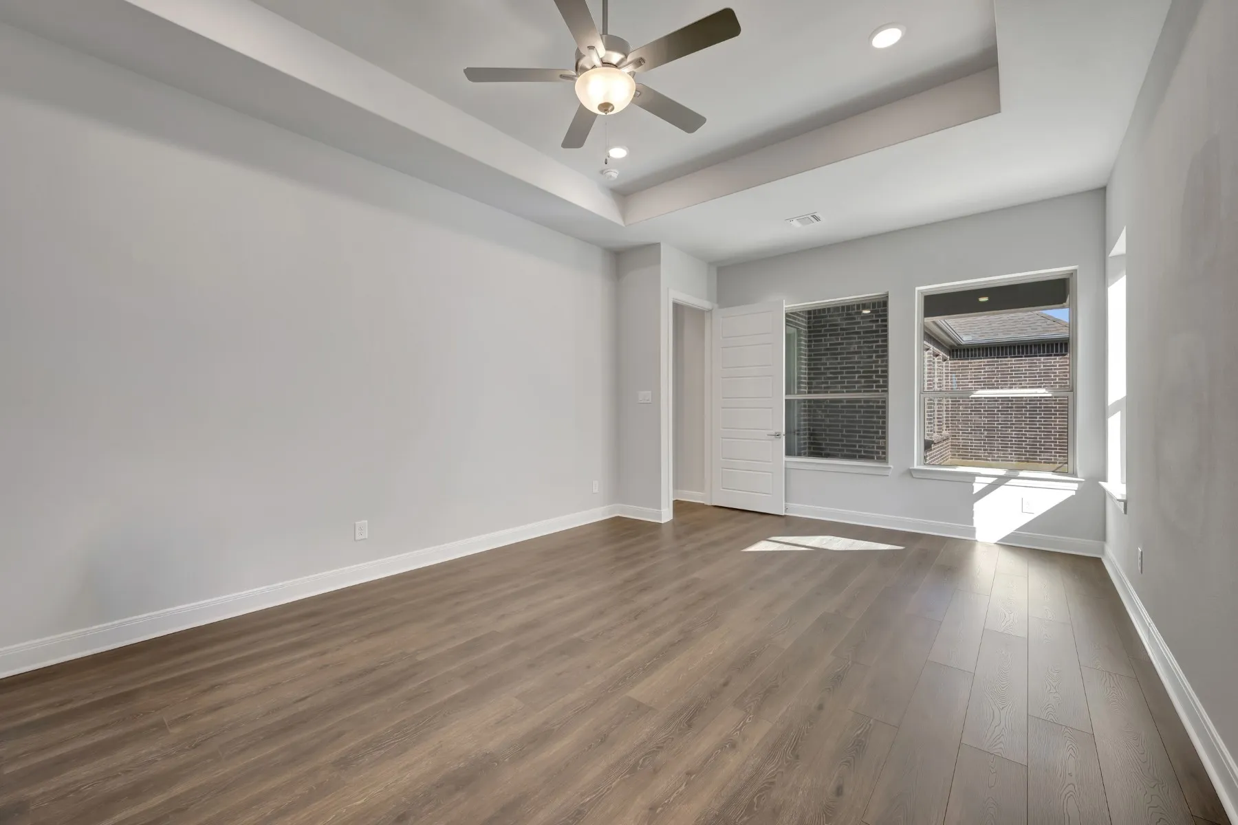 Empty room with ceiling fan, dark wood-style flooring, recessed lighting, and a tray ceiling