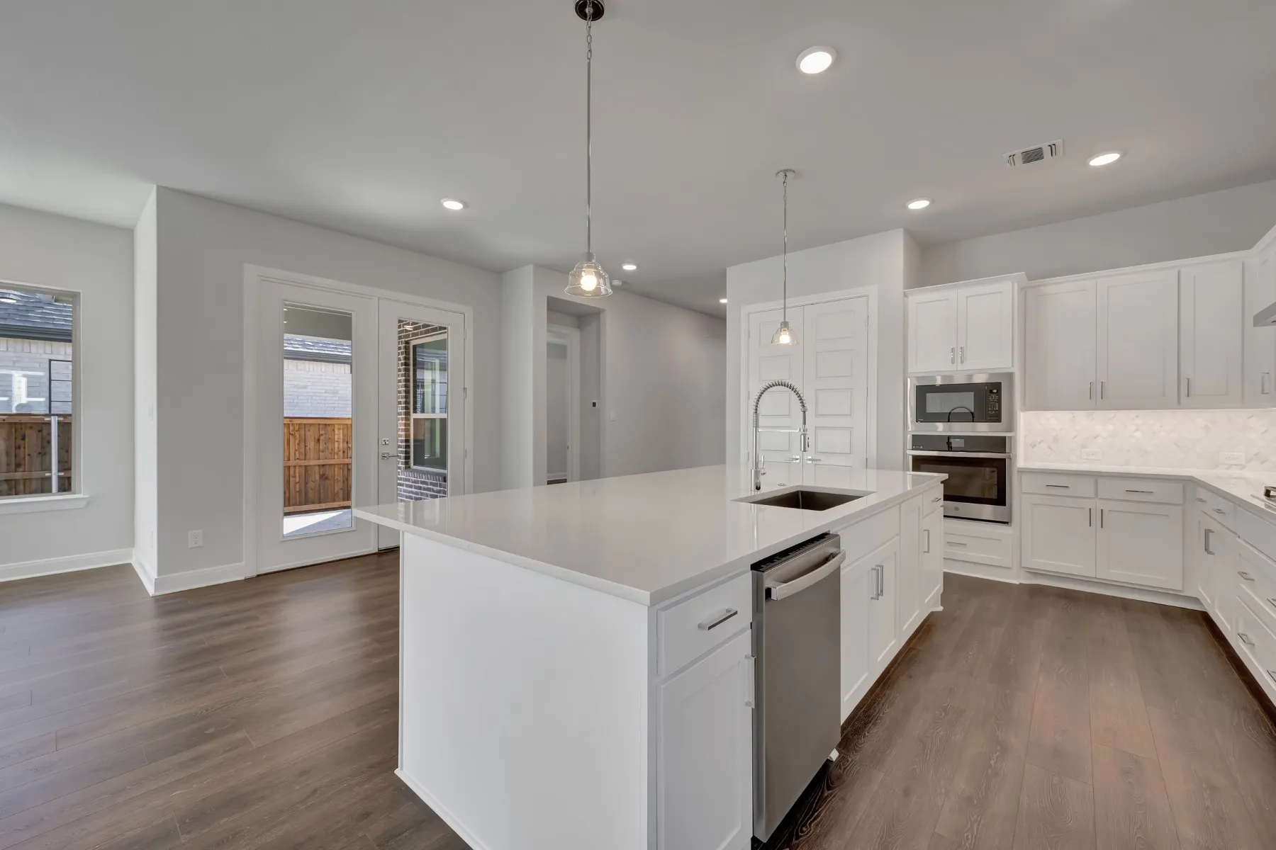 Kitchen with stainless steel appliances, white cabinets, backsplash, pendant lighting, and an island with sink
