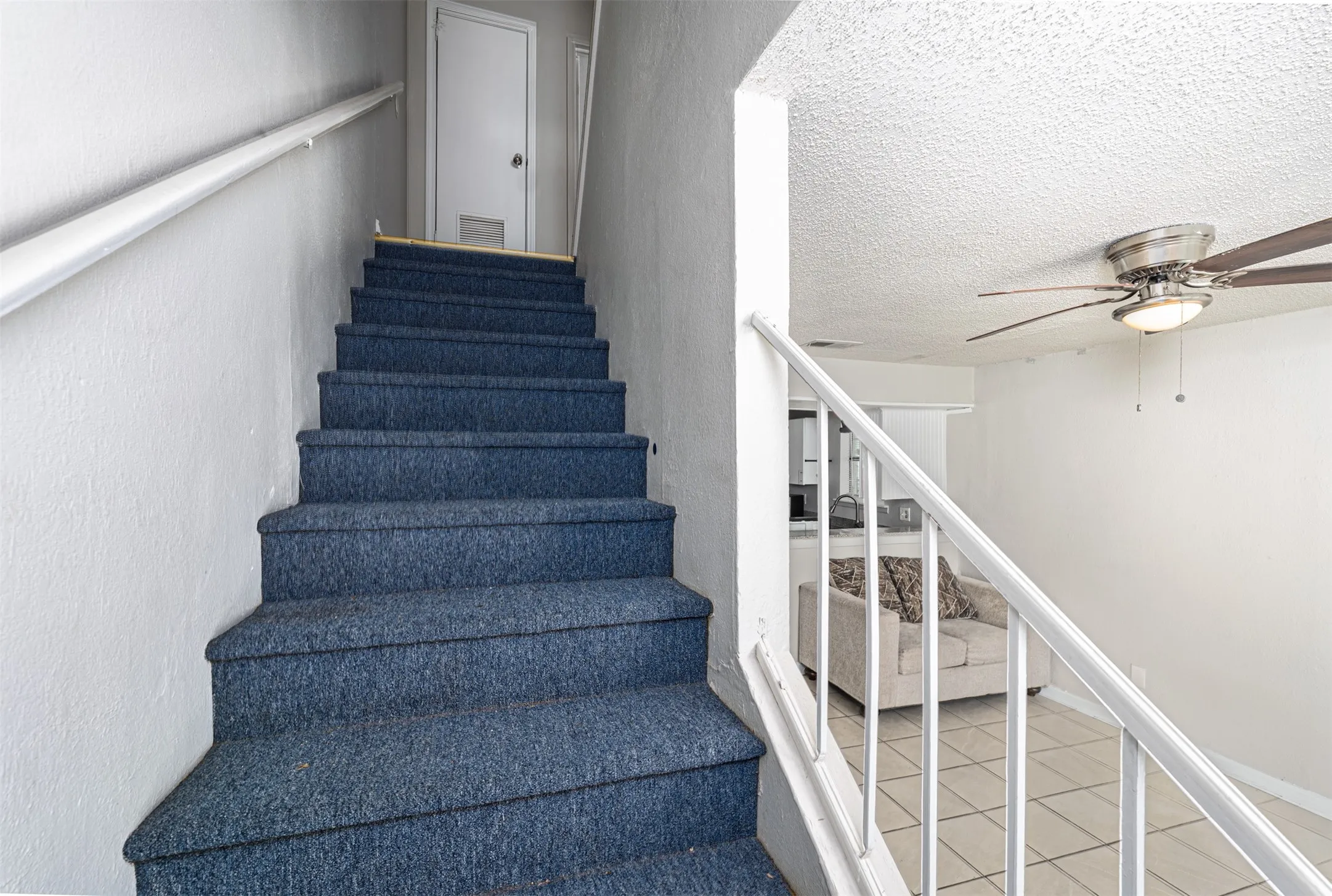 Staircase featuring a ceiling fan, a textured ceiling, and tile patterned flooring
