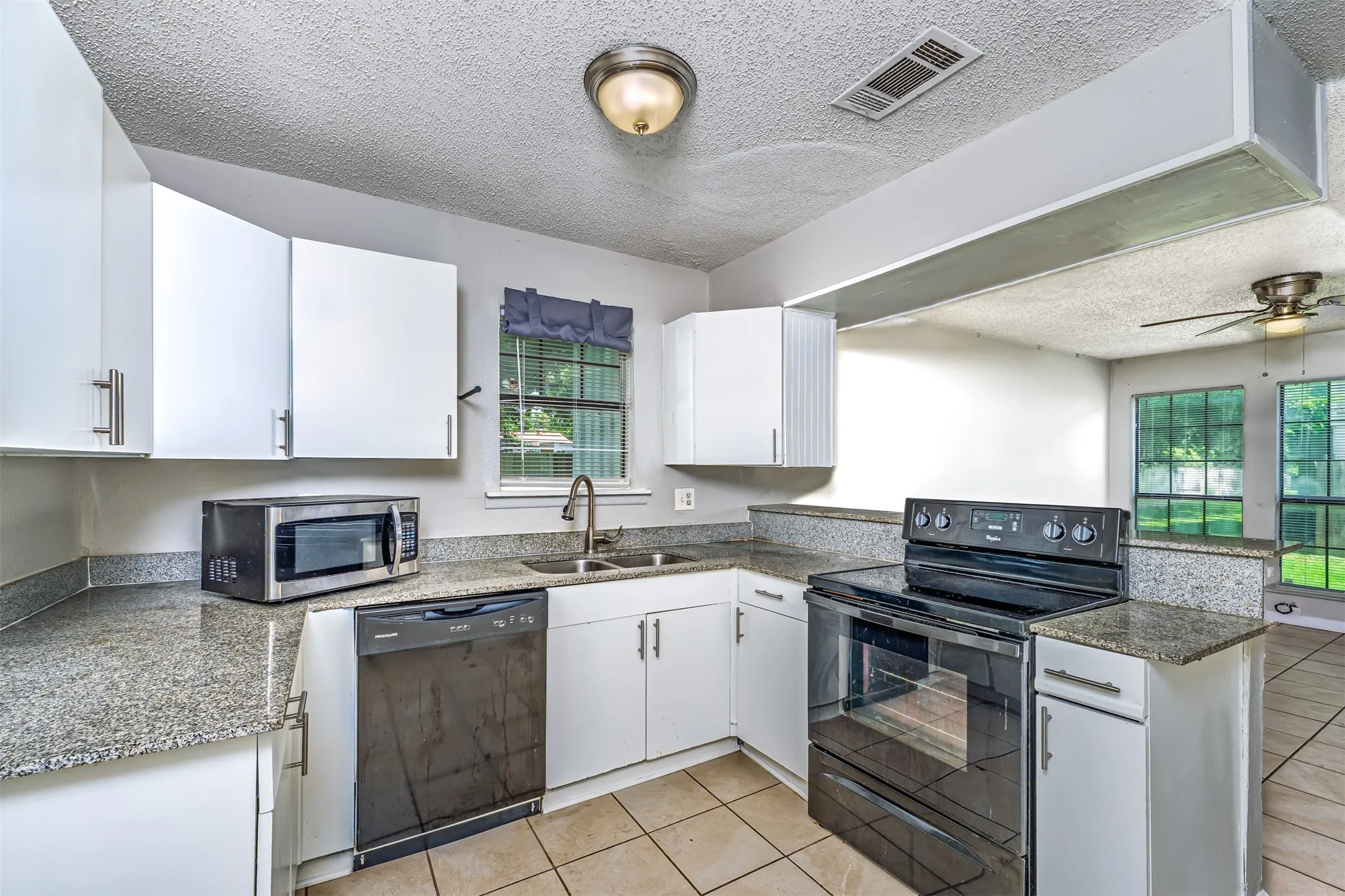 Kitchen with black appliances, a textured ceiling, white cabinetry, and light tile patterned flooring