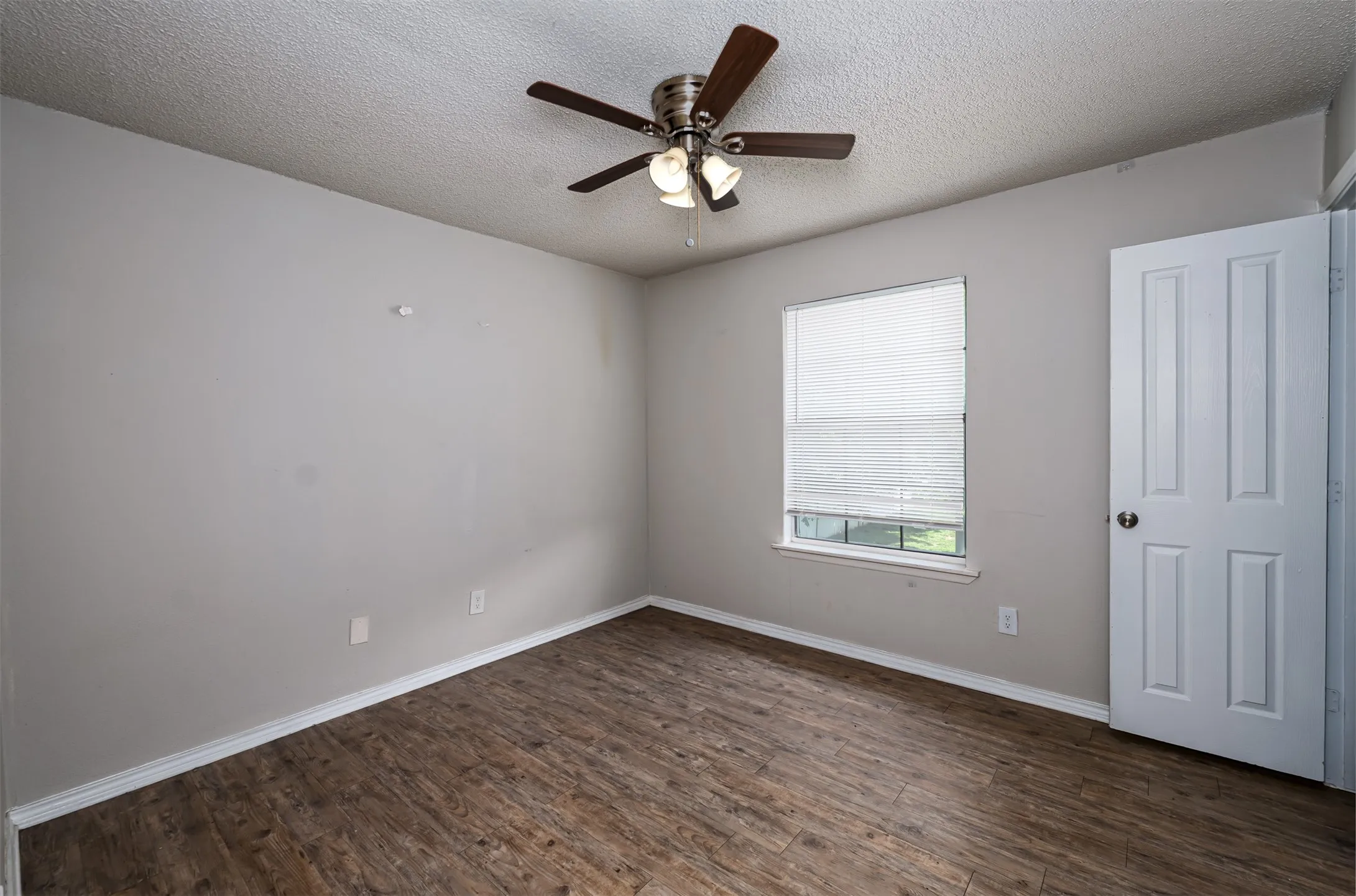 Empty room featuring a textured ceiling, dark wood-style floors, and a ceiling fan