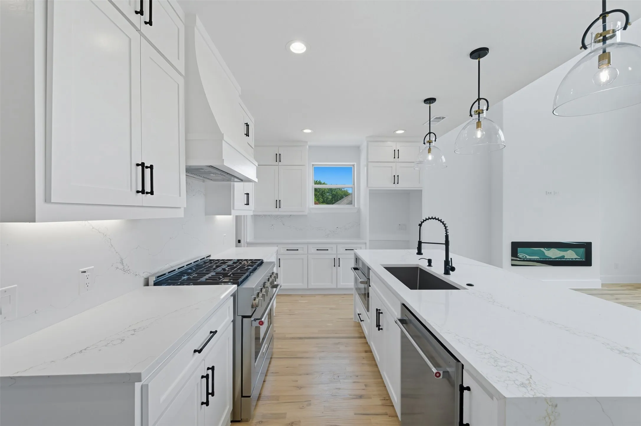 Kitchen featuring light stone countertops, appliances with stainless steel finishes, tasteful backsplash, pendant lighting, and light wood-style flooring