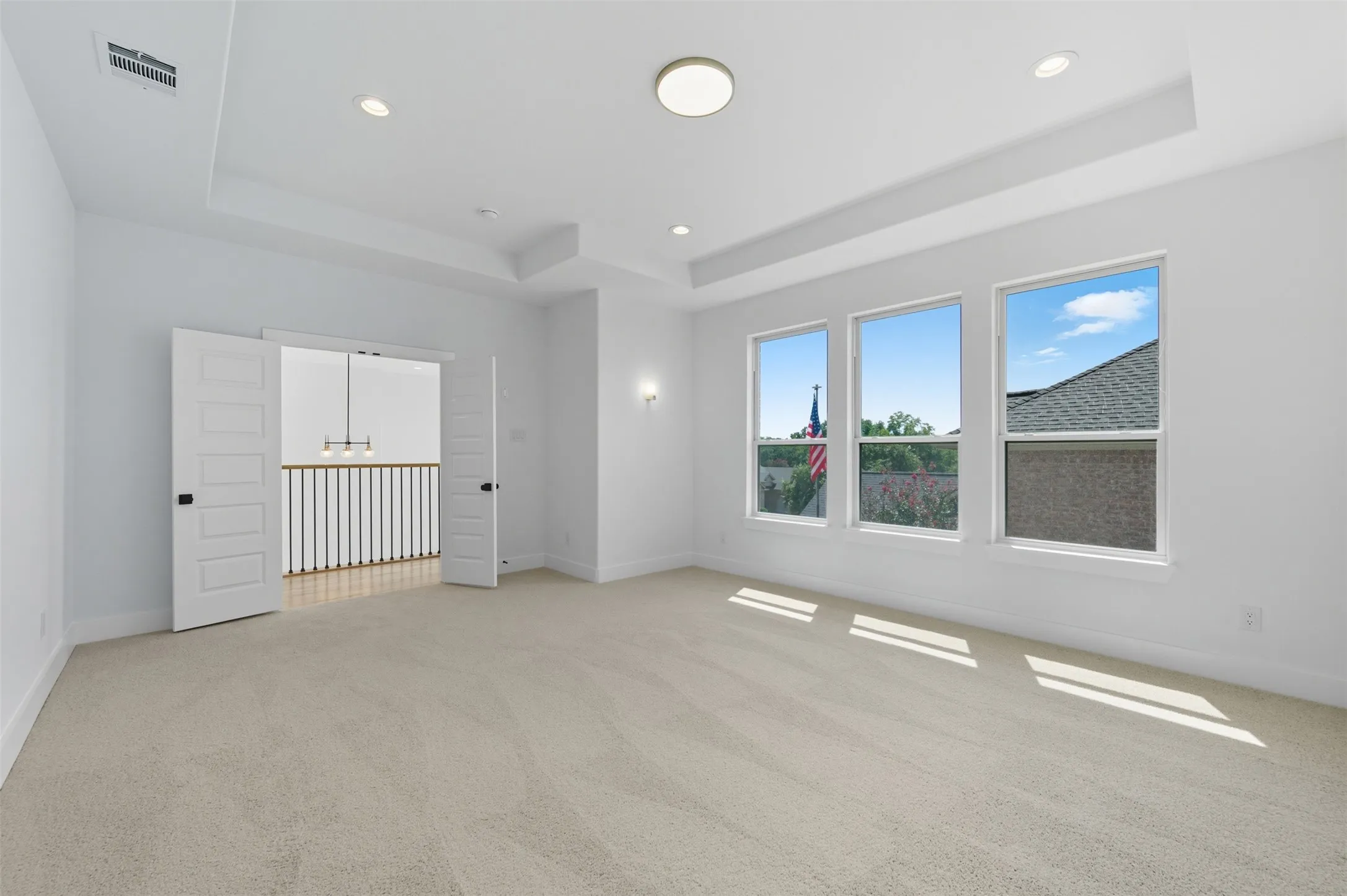 Spare room with a raised ceiling, light colored carpet, recessed lighting, and a chandelier