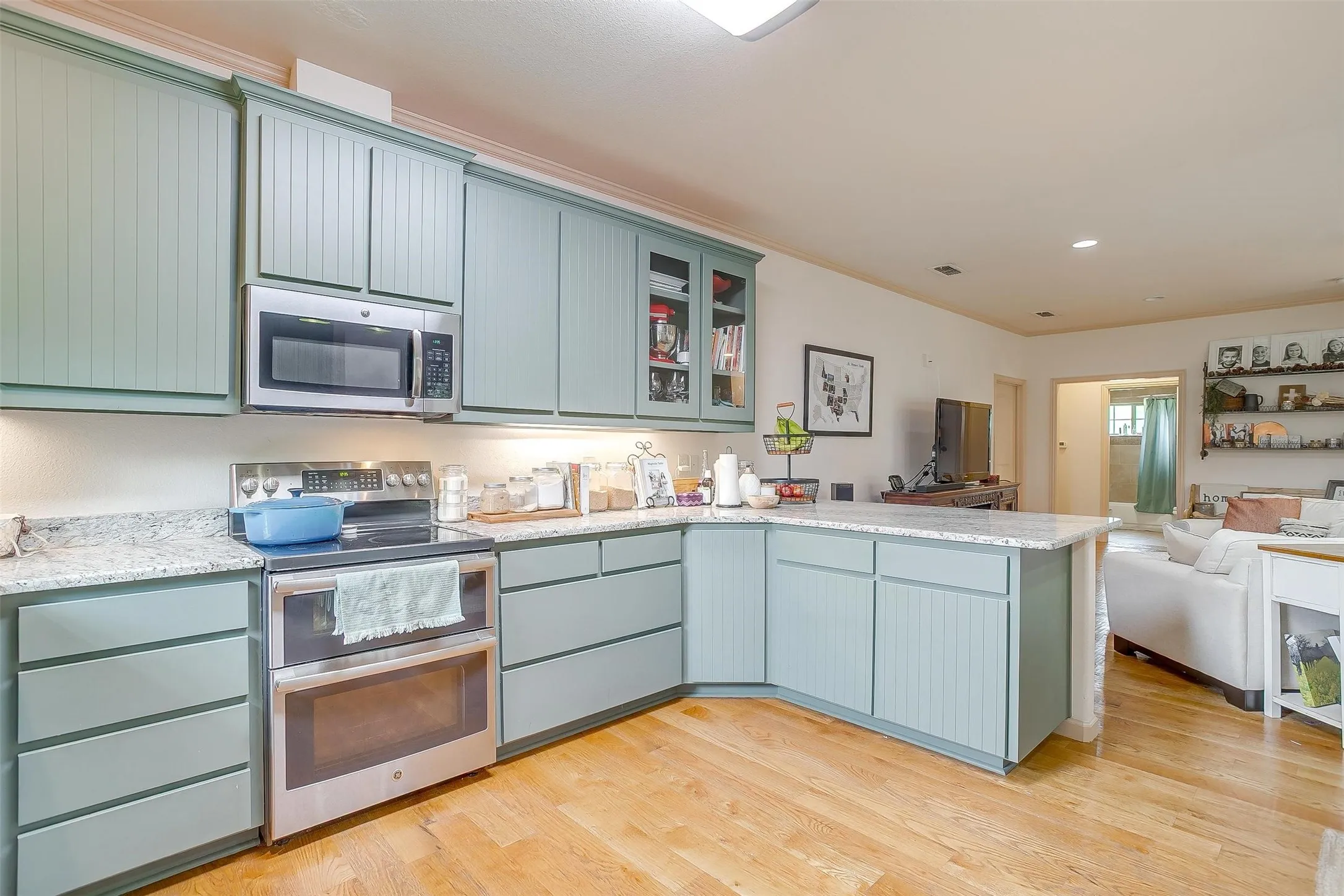 Kitchen with a peninsula, appliances with stainless steel finishes, glass insert cabinets, open floor plan, and light wood finished floors.