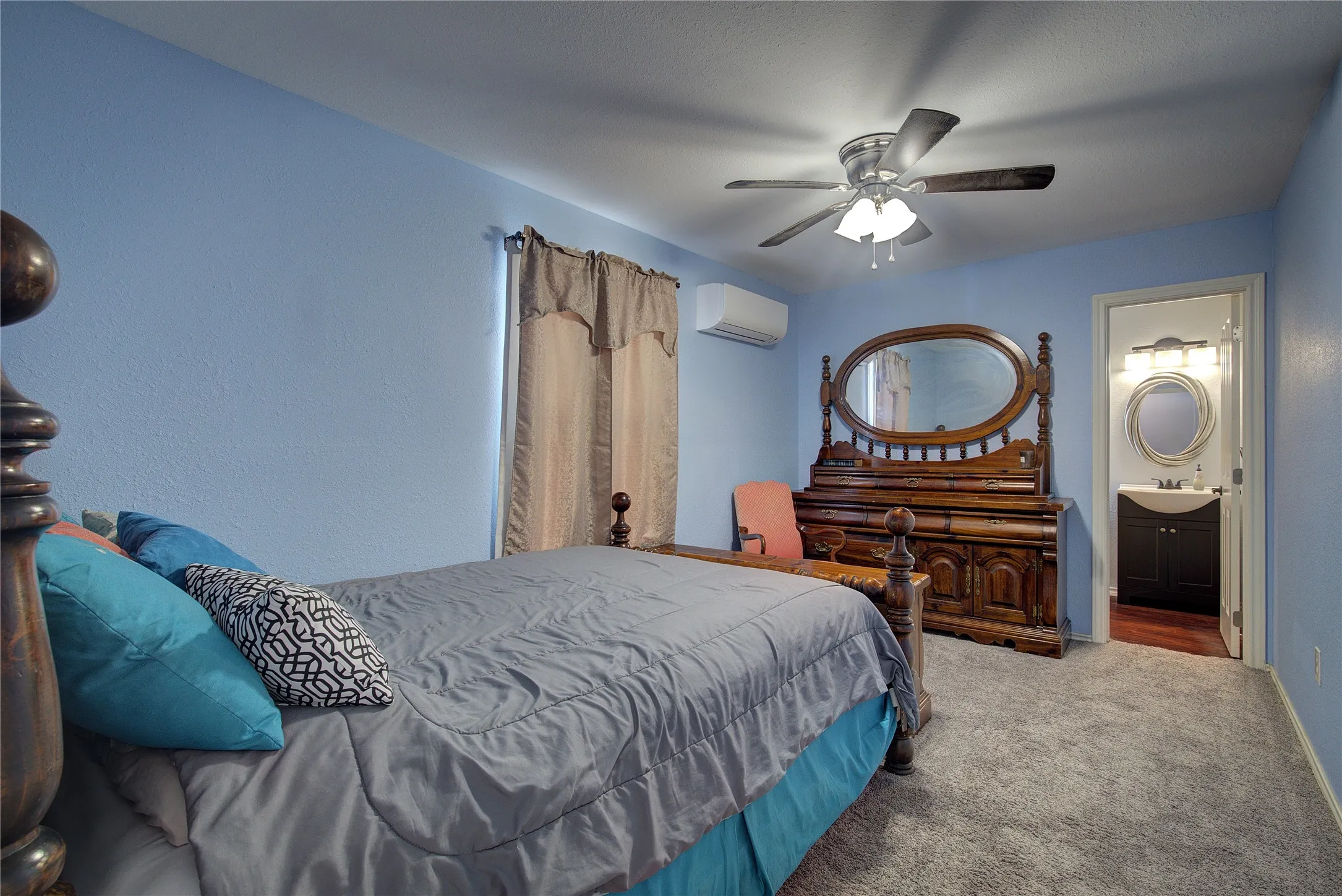 Bedroom featuring a wall mounted air conditioner, ensuite bathroom, ceiling fan, sink, and carpet floors