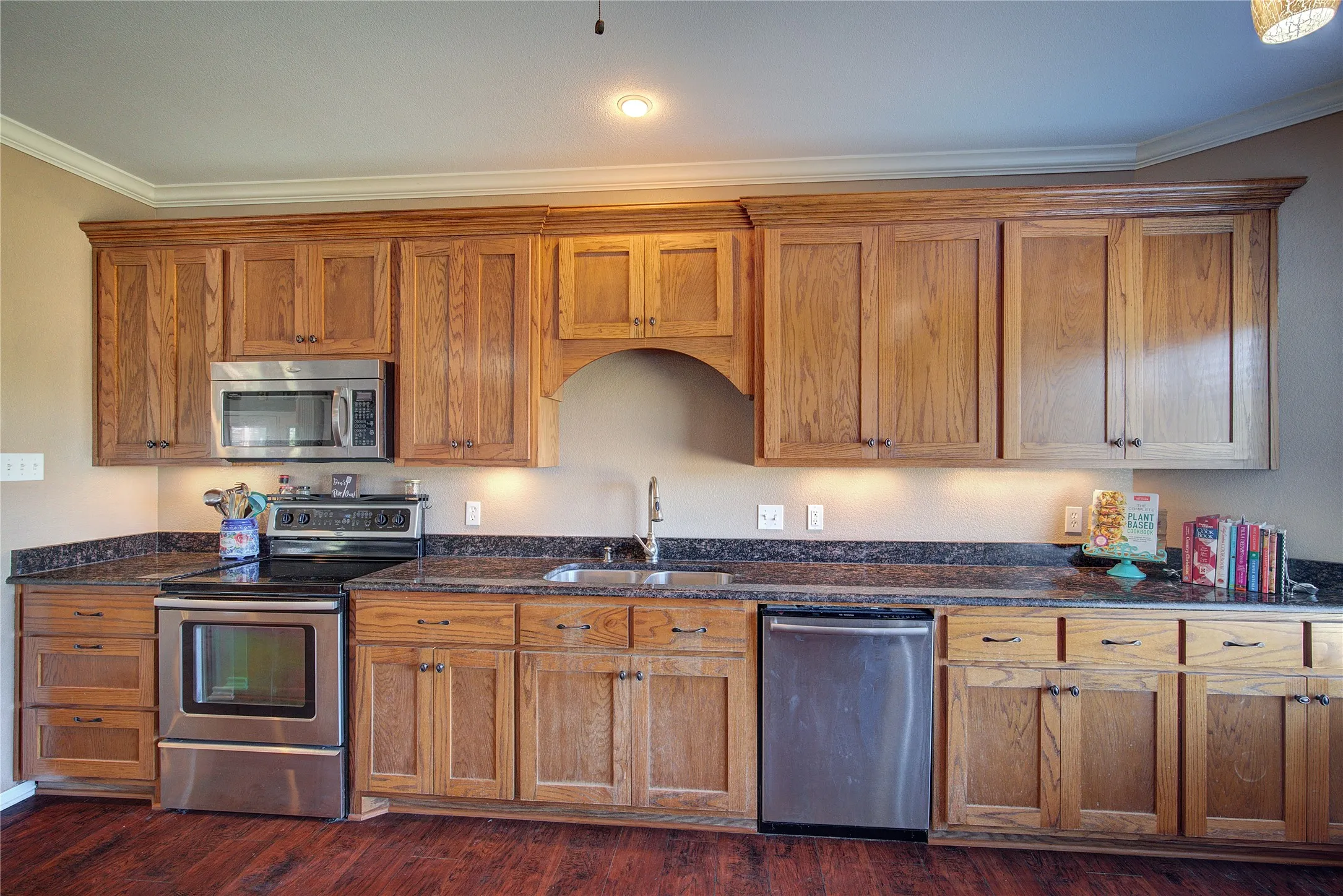 Kitchen featuring sink, dark hardwood / wood-style flooring, dark stone countertops, crown molding, and appliances with stainless steel finishes