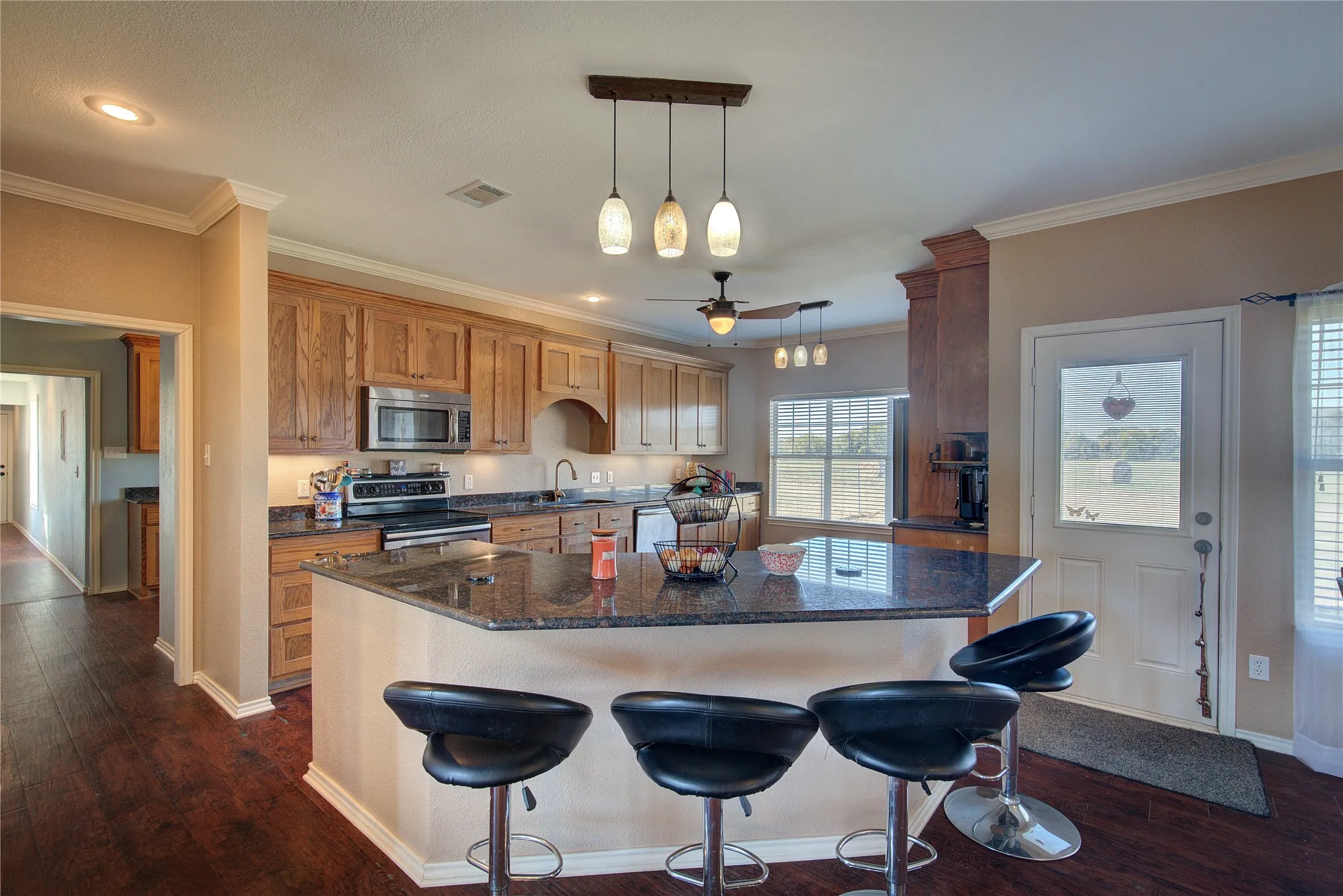 Kitchen featuring appliances with stainless steel finishes, ceiling fan, crown molding, decorative light fixtures, and dark hardwood / wood-style floors