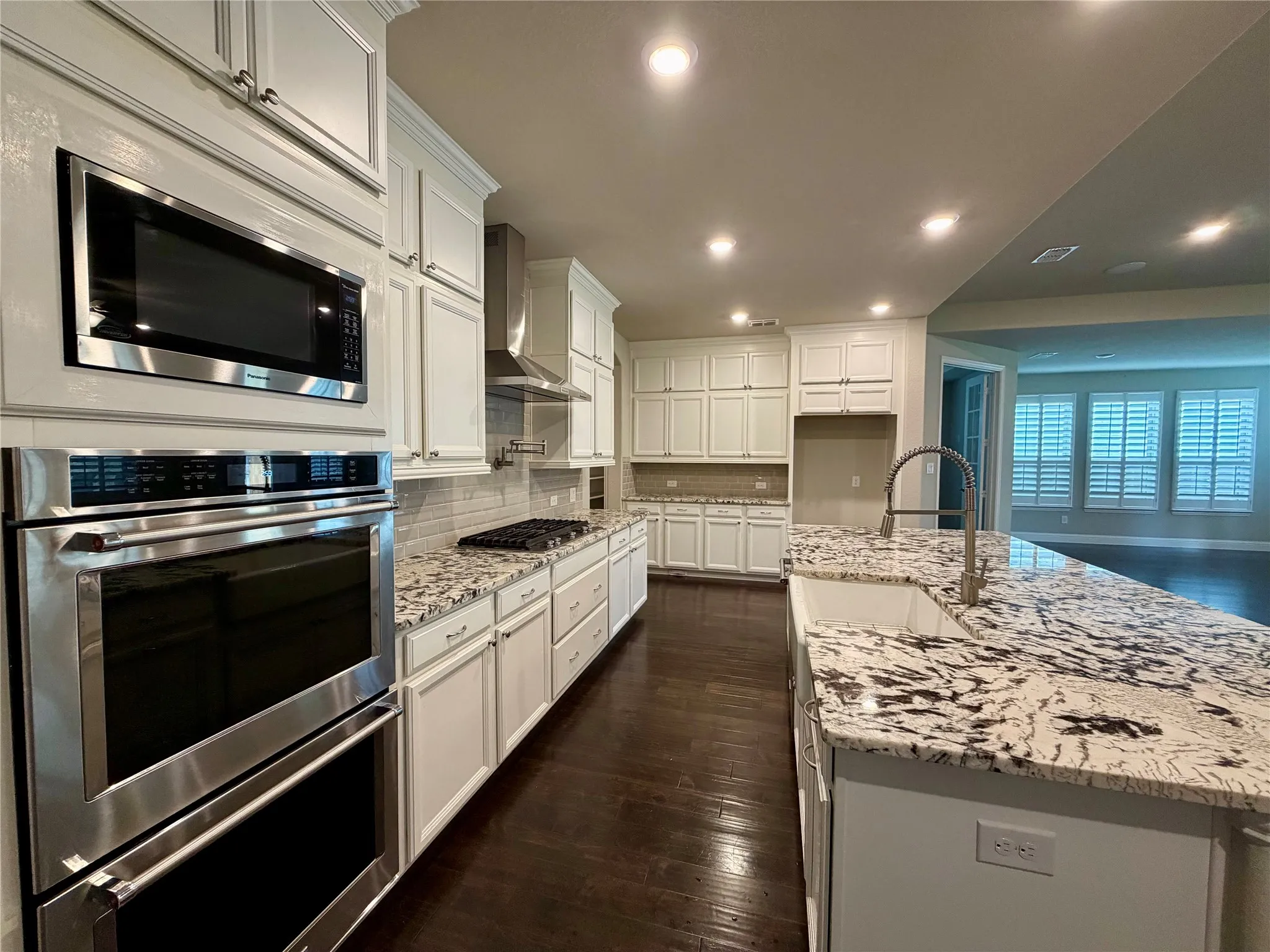 Kitchen featuring light stone counters, stainless steel appliances, dark wood-type flooring, decorative backsplash, and white cabinets