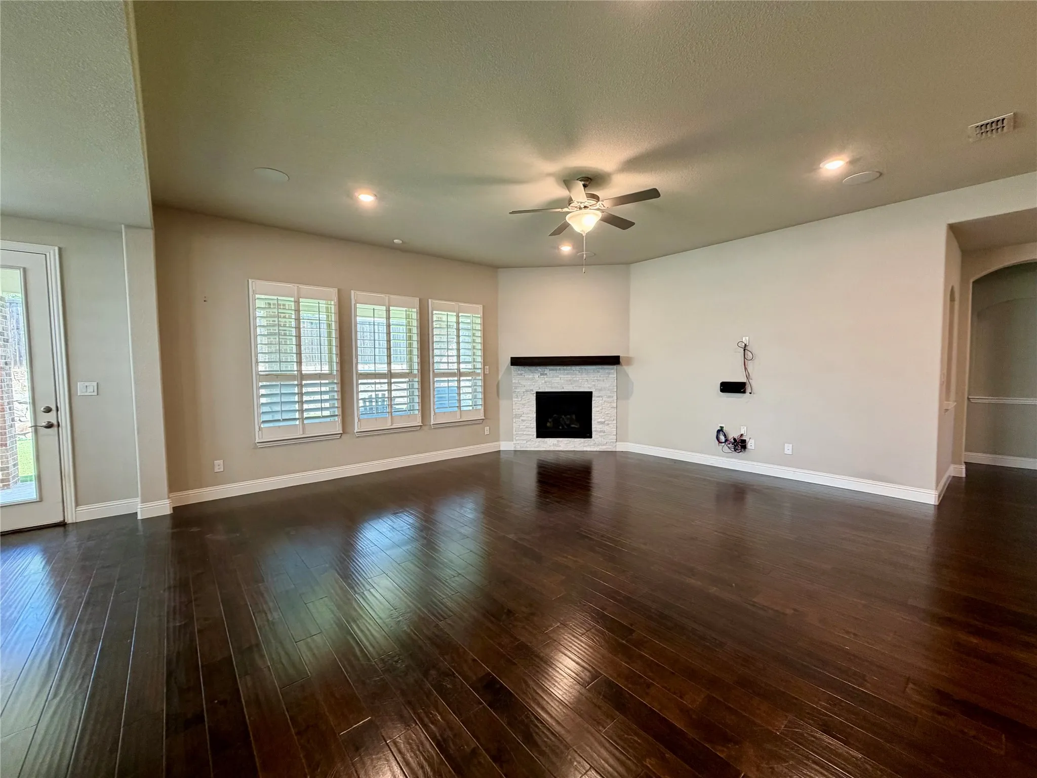 Unfurnished living room featuring dark wood-style flooring, recessed lighting, ceiling fan, arched walkways, and a stone fireplace