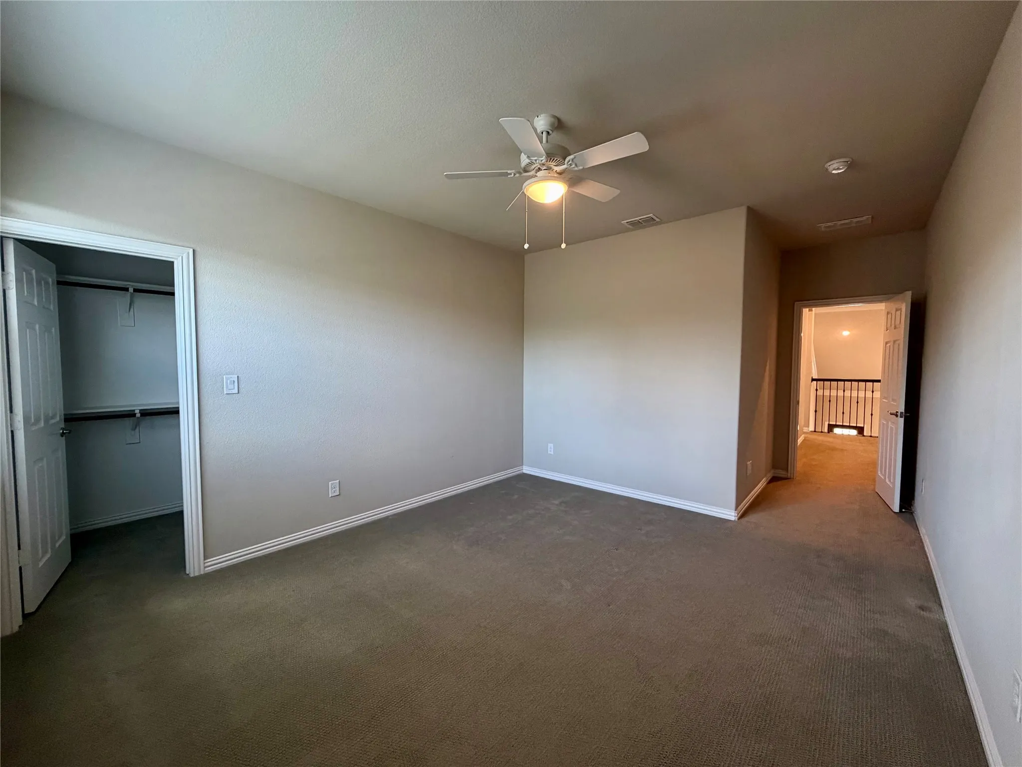 Unfurnished bedroom featuring a spacious closet, carpet, and a ceiling fan