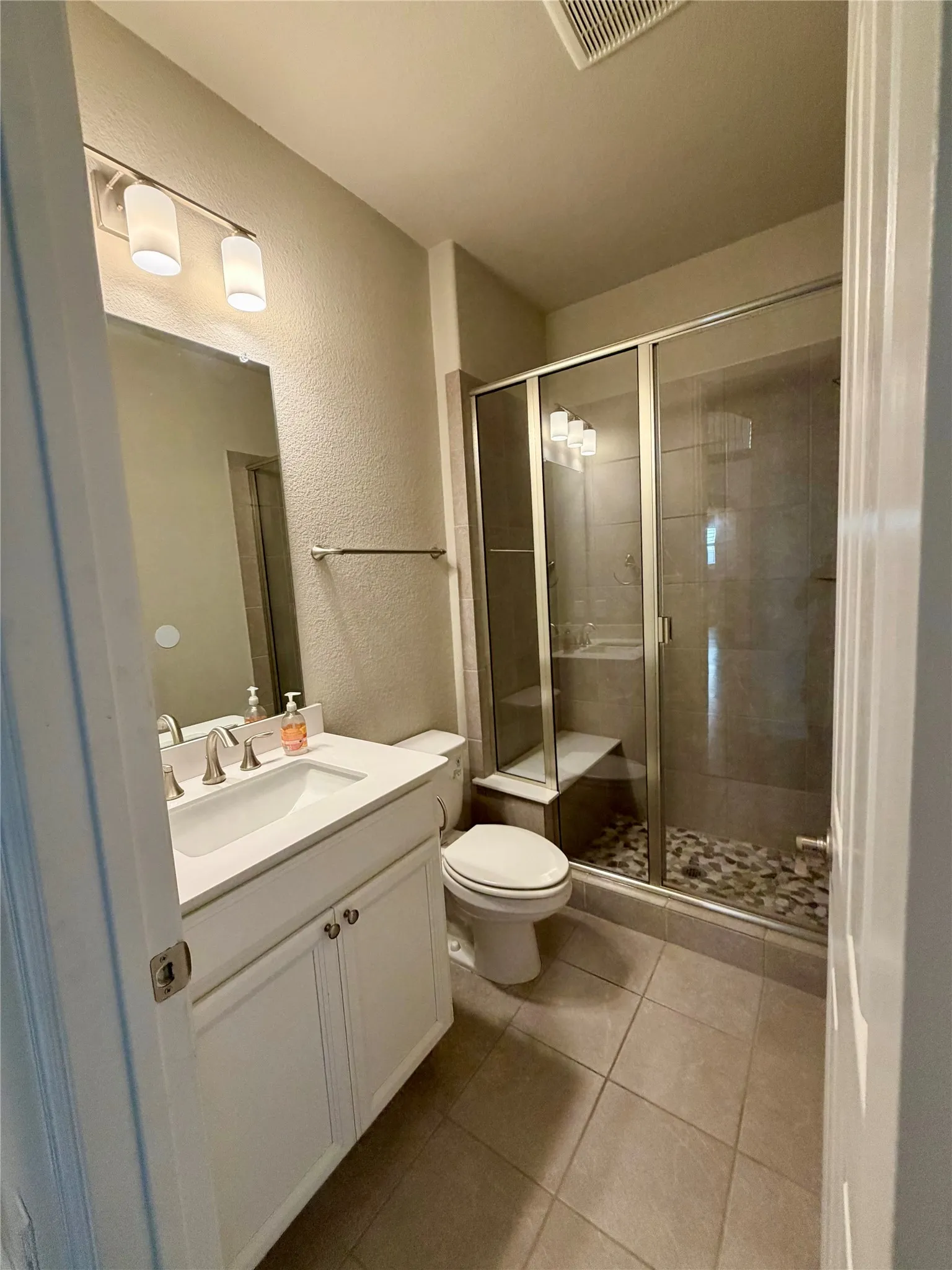 Full bathroom featuring a textured wall, a shower stall, vanity, and light tile patterned floors