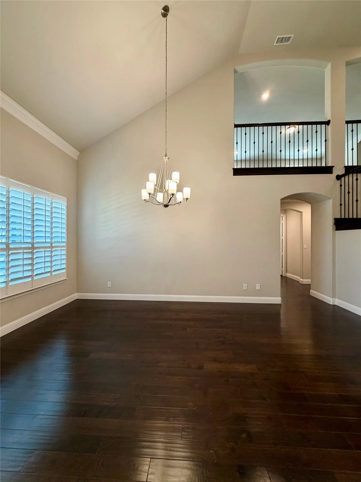 Unfurnished dining area with high vaulted ceiling, arched walkways, dark wood-style floors, and a chandelier