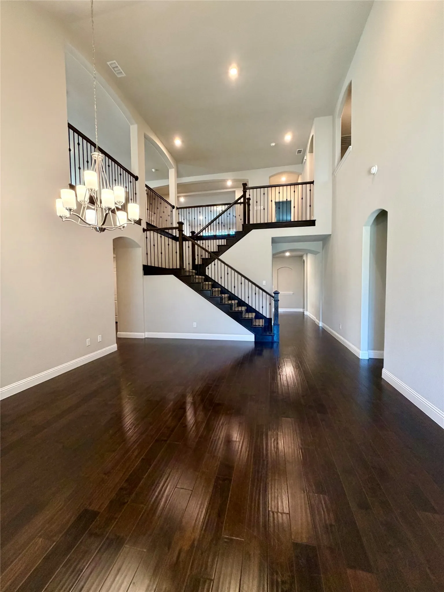 Unfurnished dining room with arched walkways, dark wood-style flooring, a towering ceiling, stairway, and a​​‌​​​​‌​​‌‌​‌‌​​​‌‌​‌​‌​‌​​​‌​​ chandelier