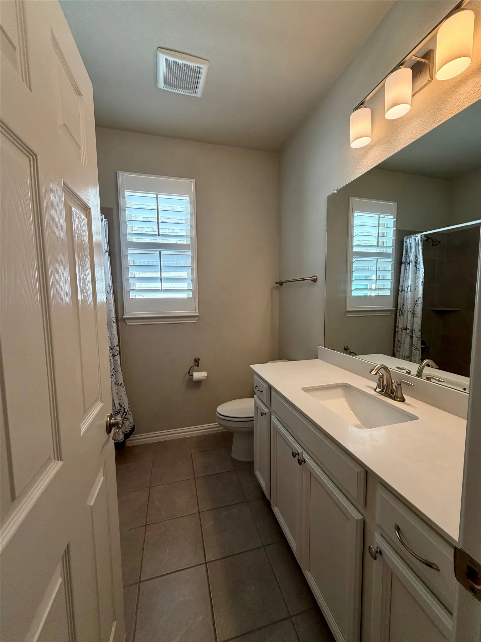 Bathroom with vanity, dark tile patterned flooring, healthy amount of natural light, and a shower with curtain