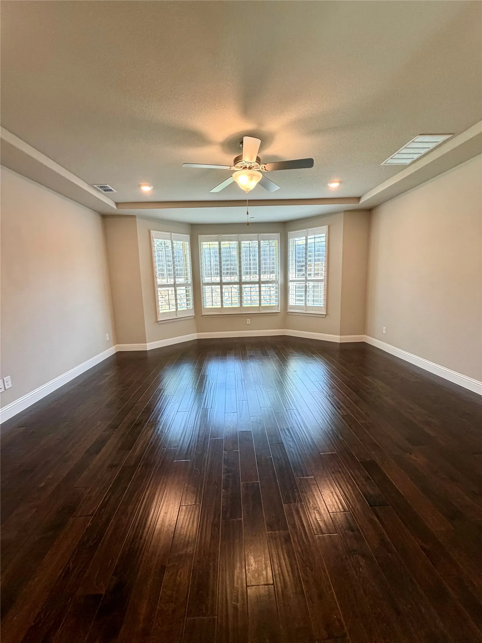 Primary bedroom featuring dark wood-style floors, a ceiling fan, a textured ceiling, and a tray ceiling