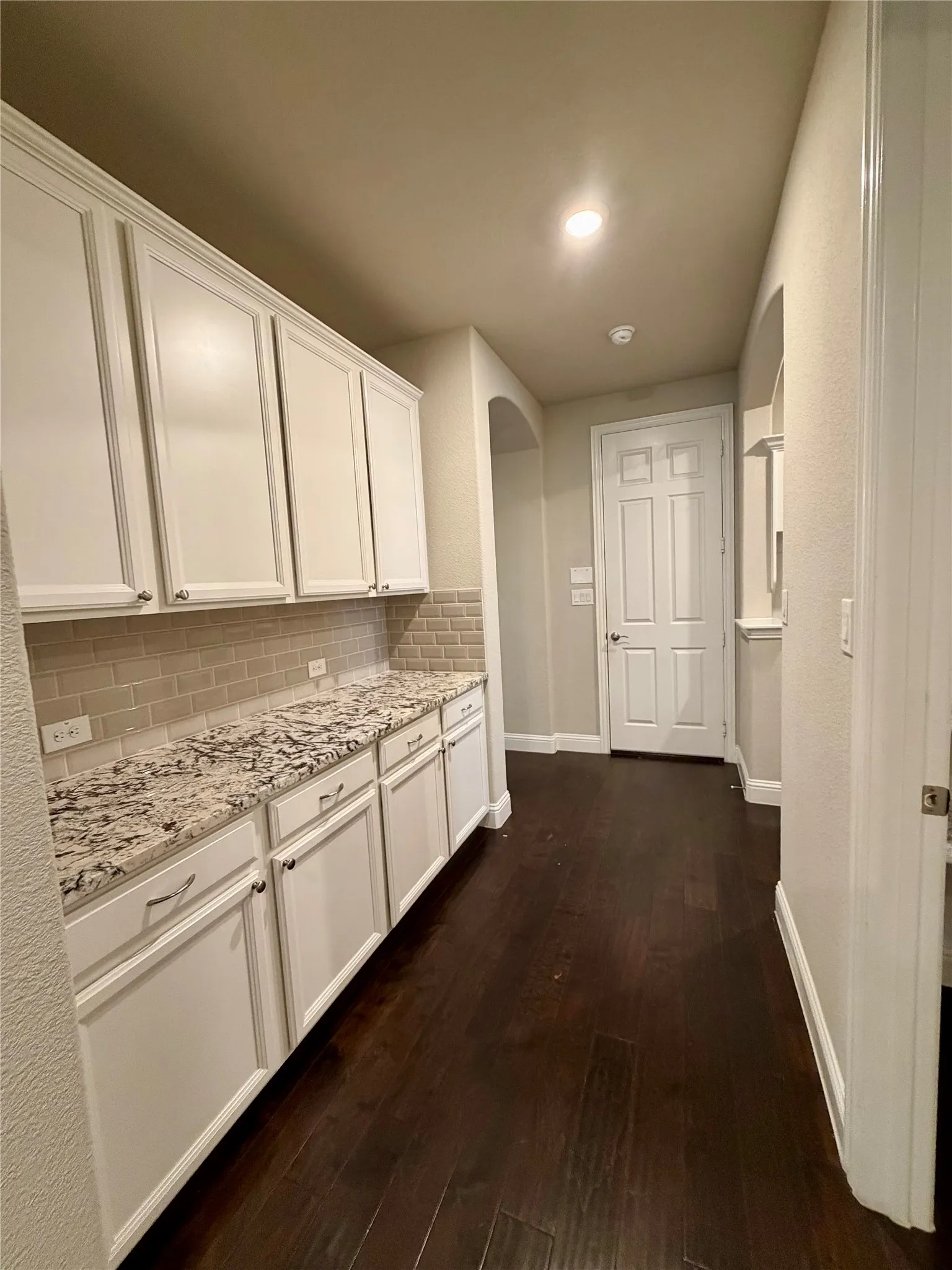 Coffee bar featuring dark wood-style floors, white cabinets, light stone counters, tasteful backsplash, and arched walkways