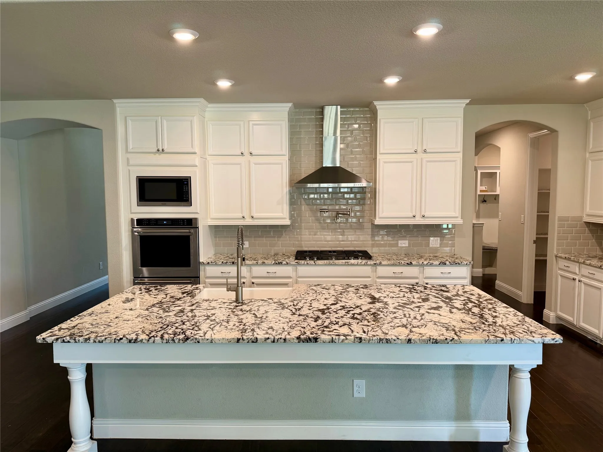 Kitchen with arched walkways, decorative backsplash, light stone countertops, appliances with stainless steel finishes, and dark wood-type flooring