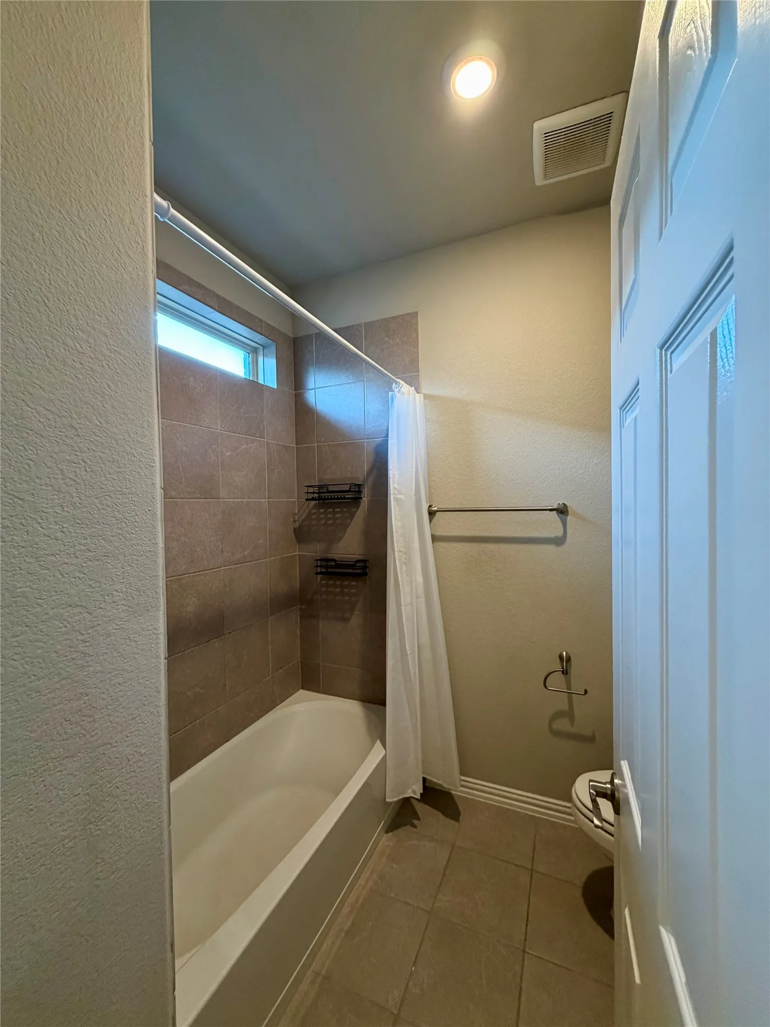 Full bathroom with tile patterned flooring, shower / bath combo with shower curtain, and a textured wall