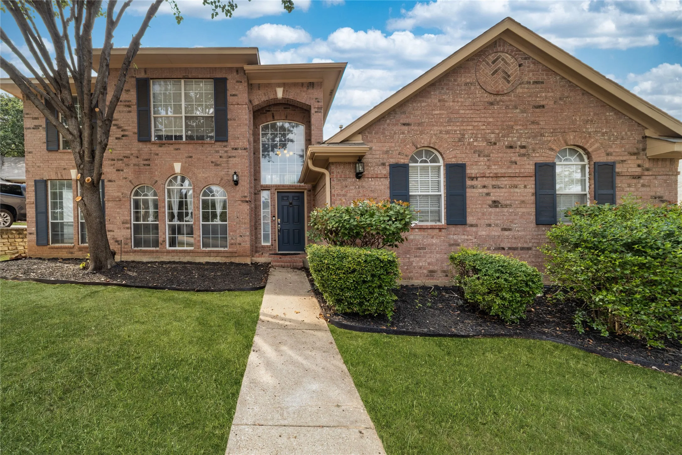 View of front of property featuring a front lawn and brick siding, mature manicured trees.