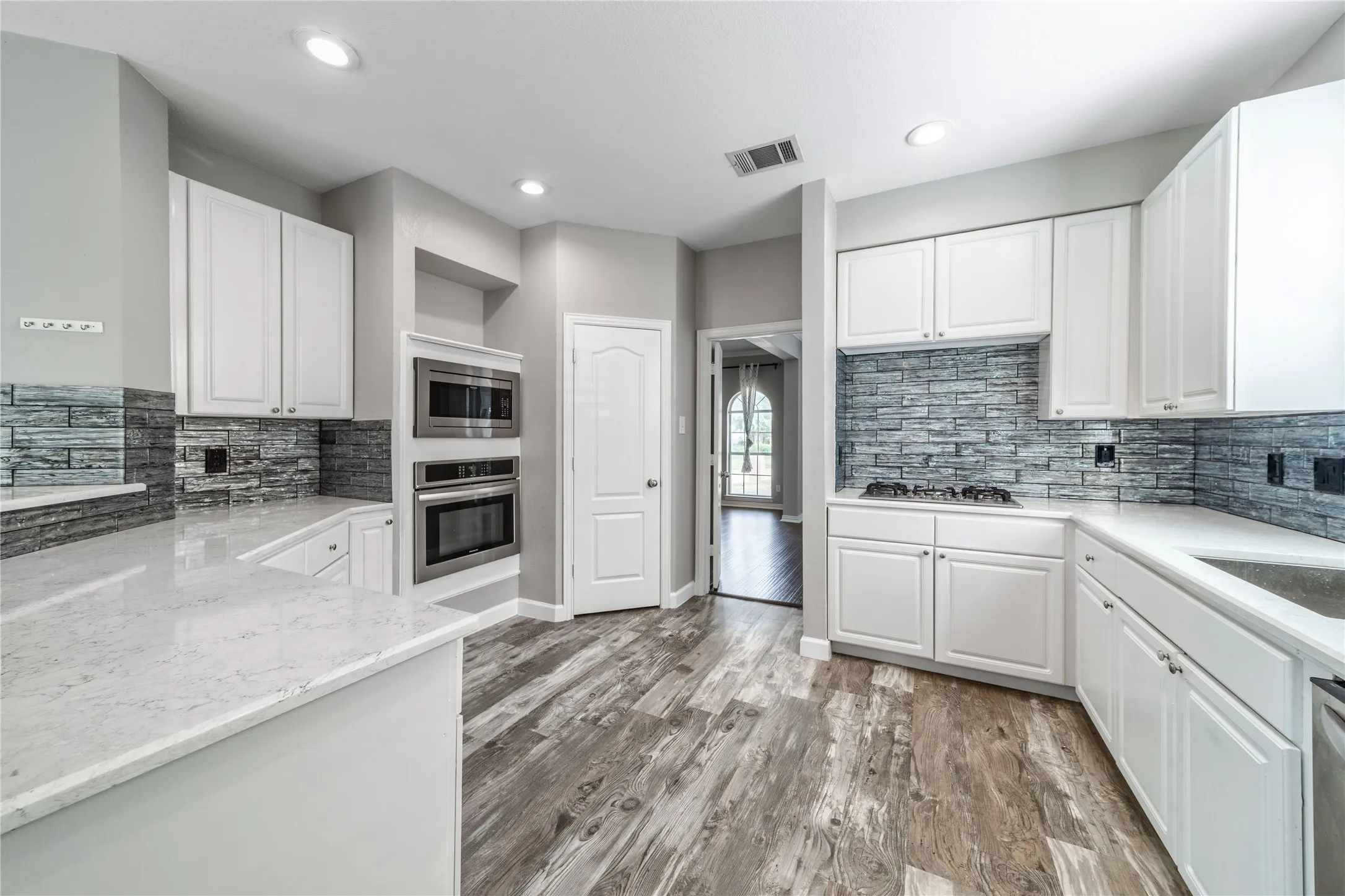 Kitchen featuring backsplash, white cabinets, light stone counters, appliances with stainless steel finishes, and recessed lighting
