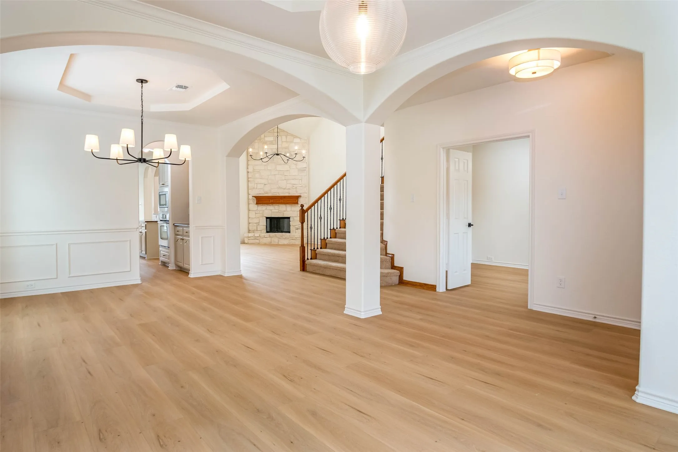 Unfurnished dining area featuring a chandelier, arched walkways, a stone fireplace, light wood-style flooring, and ornamental molding