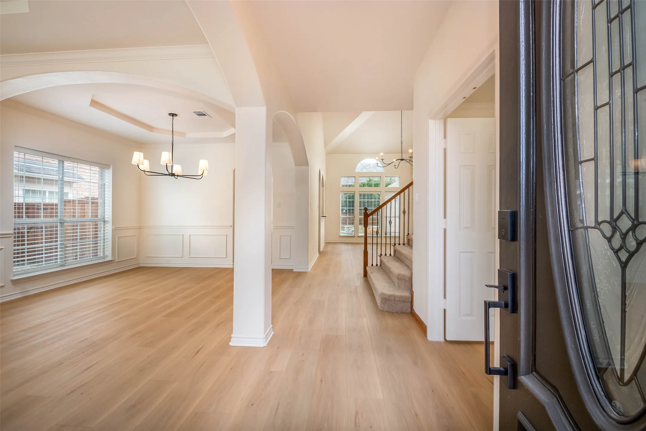 Entryway featuring a chandelier, light wood-style floors, a raised ceiling, a decorative wall, and stairway