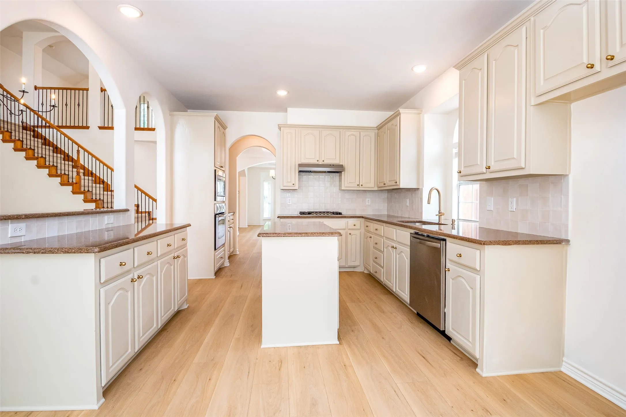 Kitchen featuring dark stone counters, a center island, cream cabinetry, light wood-style floors, and arched walkways