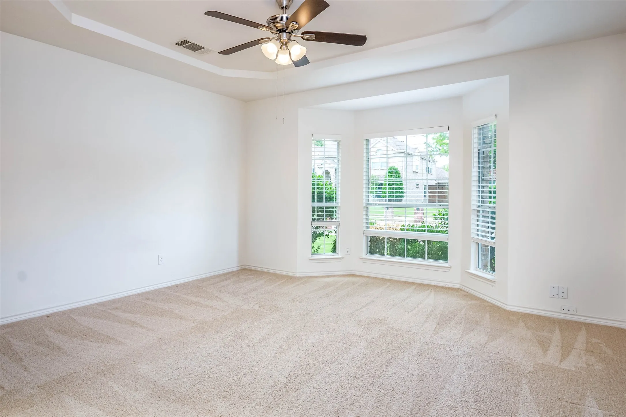Empty room with a tray ceiling, light carpet, and a ceiling fan