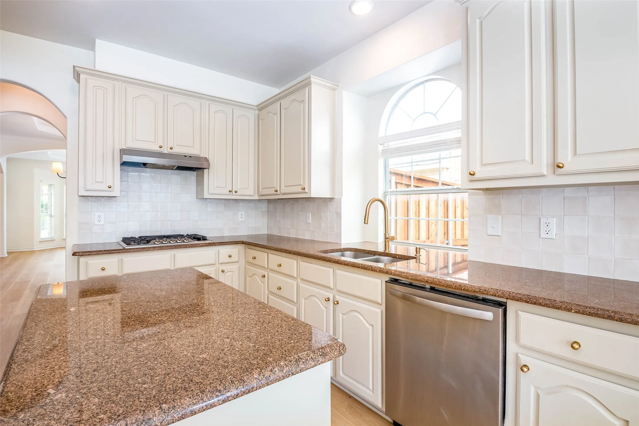 Kitchen with arched walkways, stainless steel appliances, dark stone countertops, tasteful backsplash, and cream cabinetry