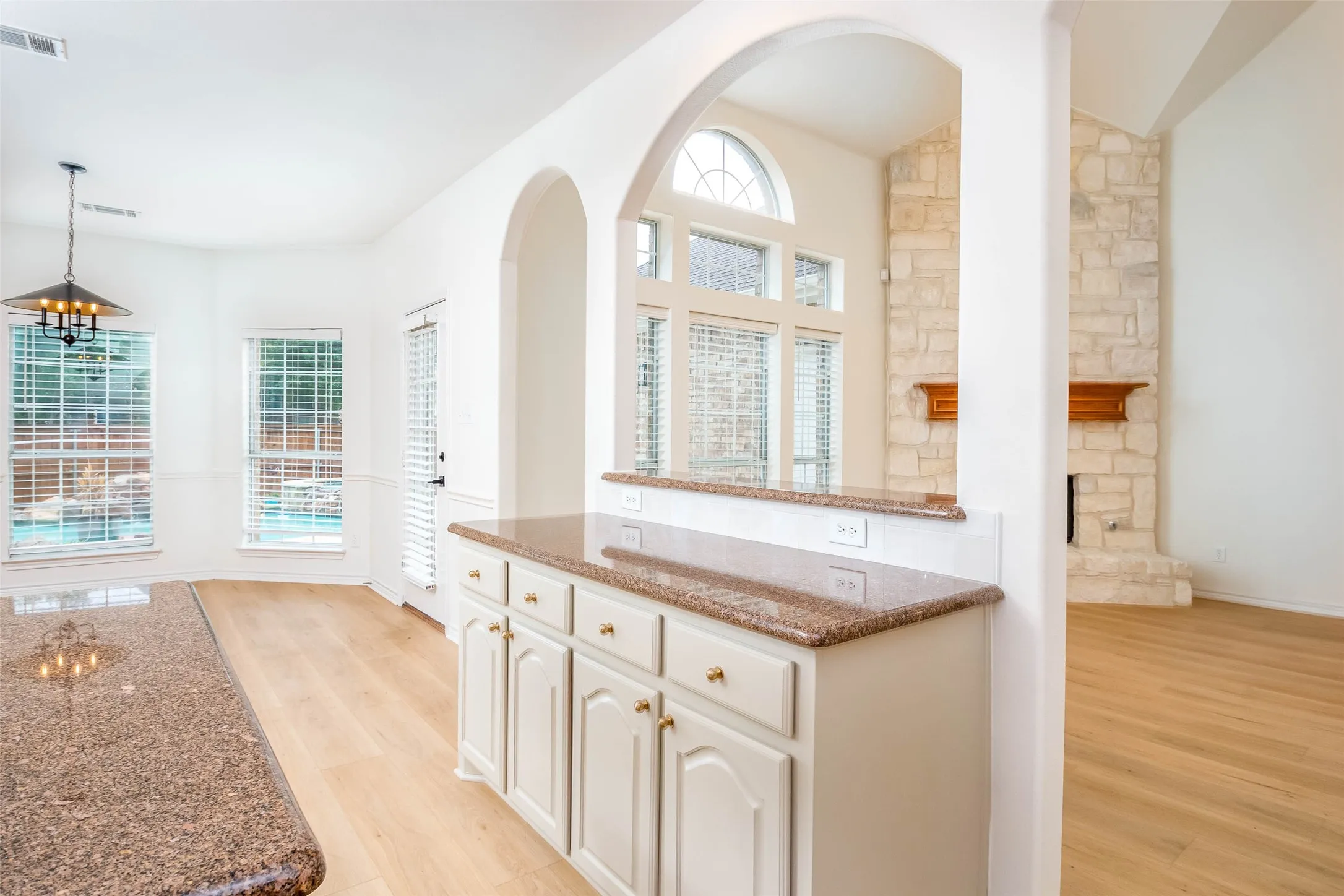 Kitchen with dark stone countertops, light wood-type flooring, decorative light fixtures, white cabinetry, and a chandelier