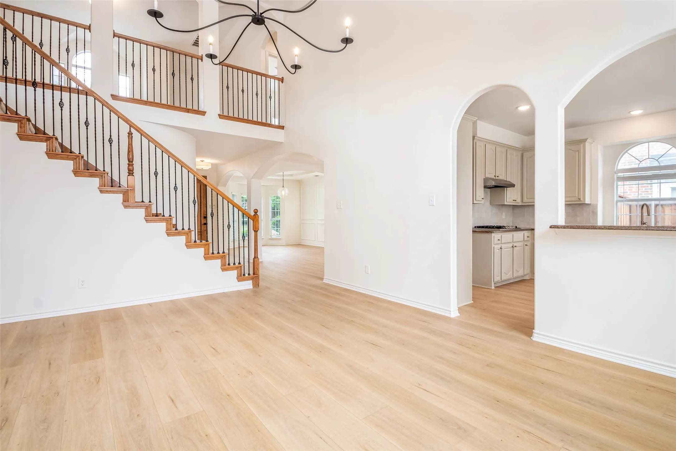 Unfurnished living room featuring arched walkways, light wood finished floors, stairway, recessed lighting, and a chandelier