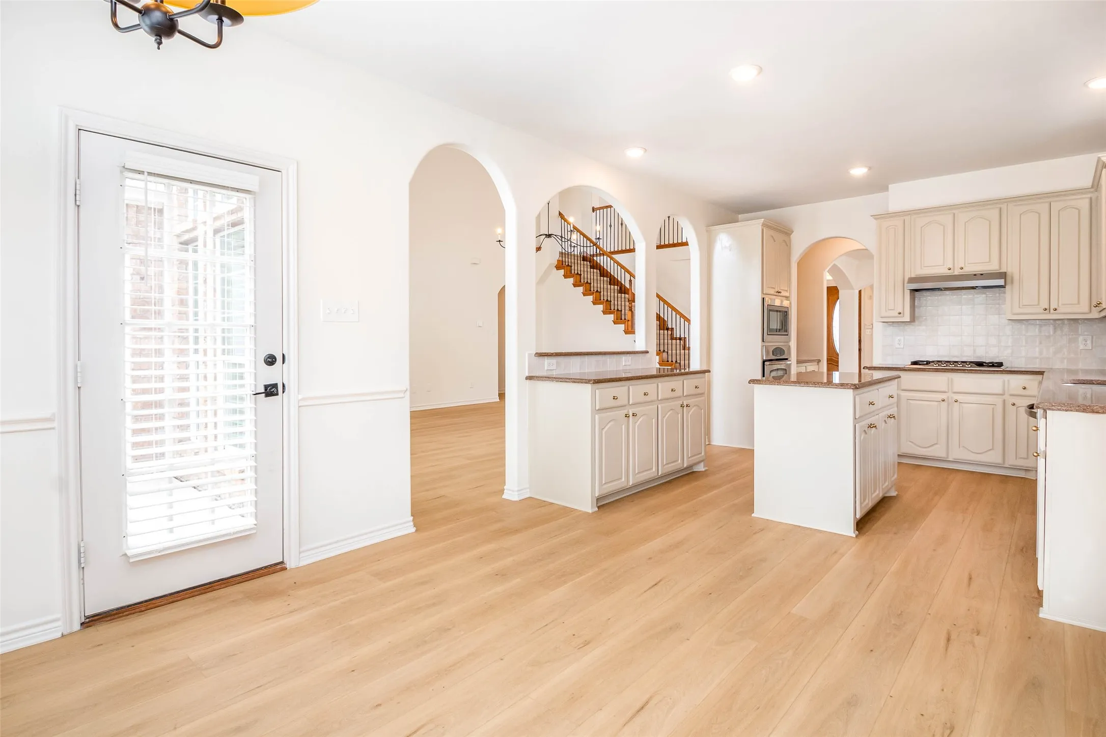 Kitchen with cream cabinetry, decorative backsplash, a kitchen island, arched walkways, and light wood-type flooring