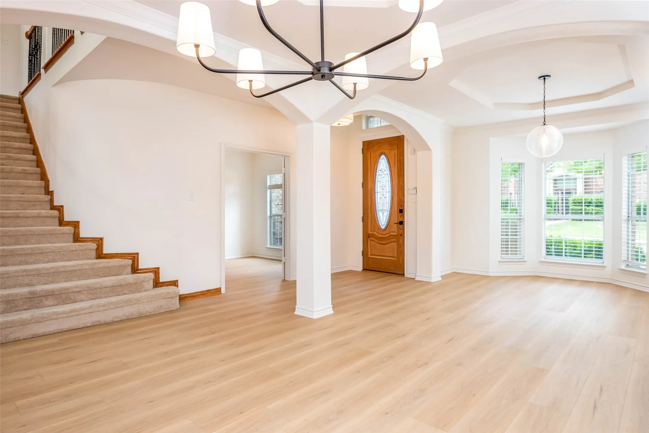 Entryway with light wood-style floors, ornamental molding, a tray ceiling, a chandelier, and stairway