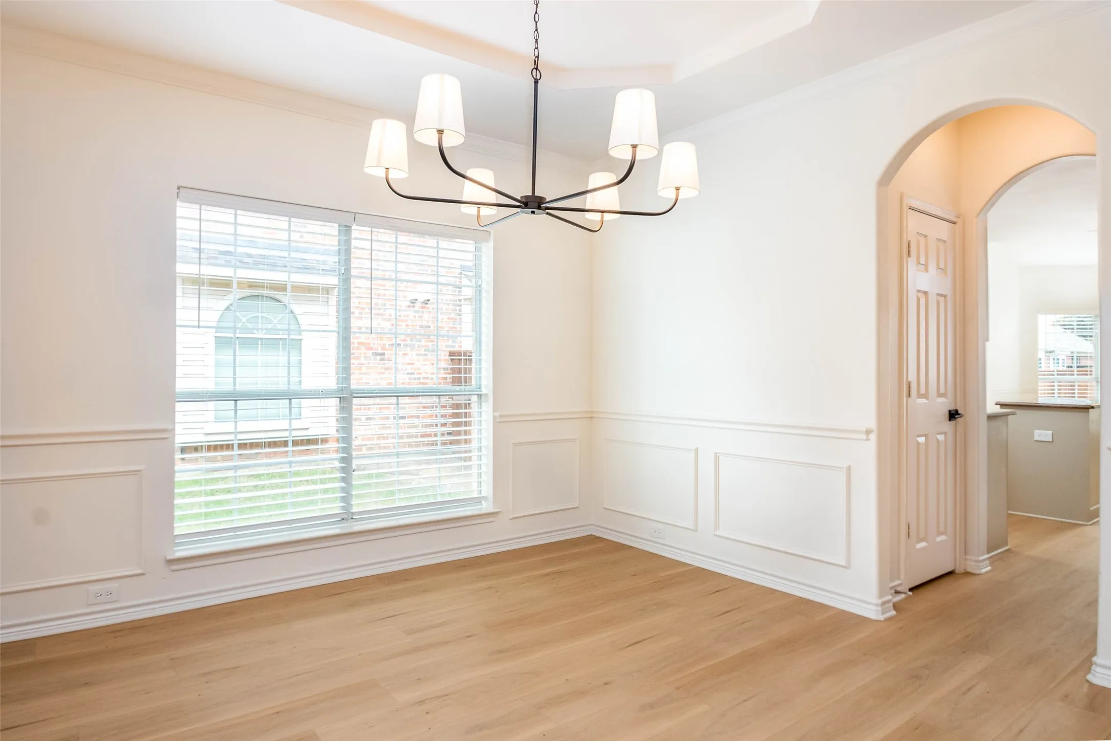 Unfurnished dining area with crown molding, light wood finished floors, arched walkways, a decorative wall, and wainscoting