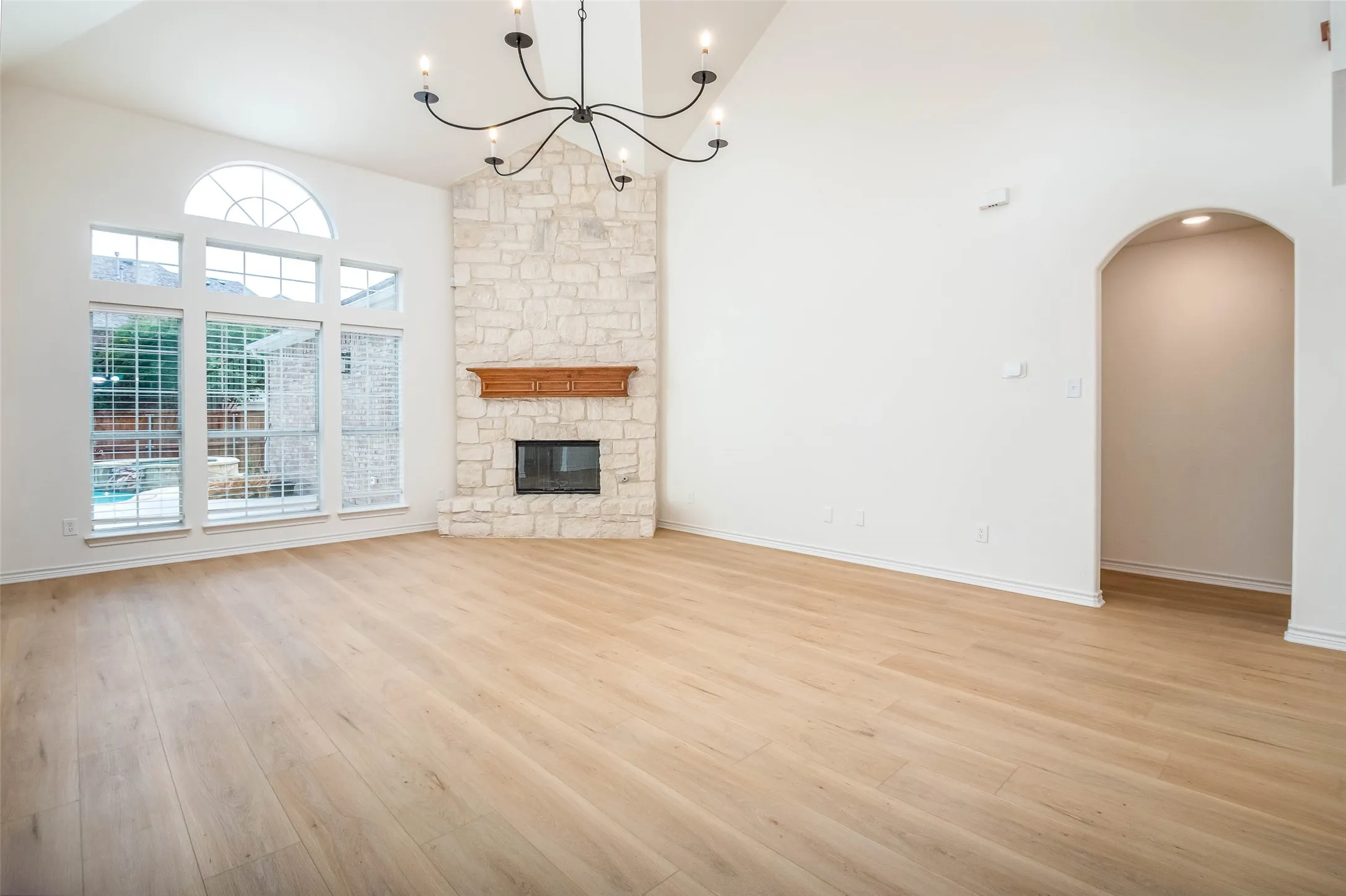 Unfurnished living room with light wood-type flooring, arched walkways, high vaulted ceiling, a chandelier, and a stone fireplace