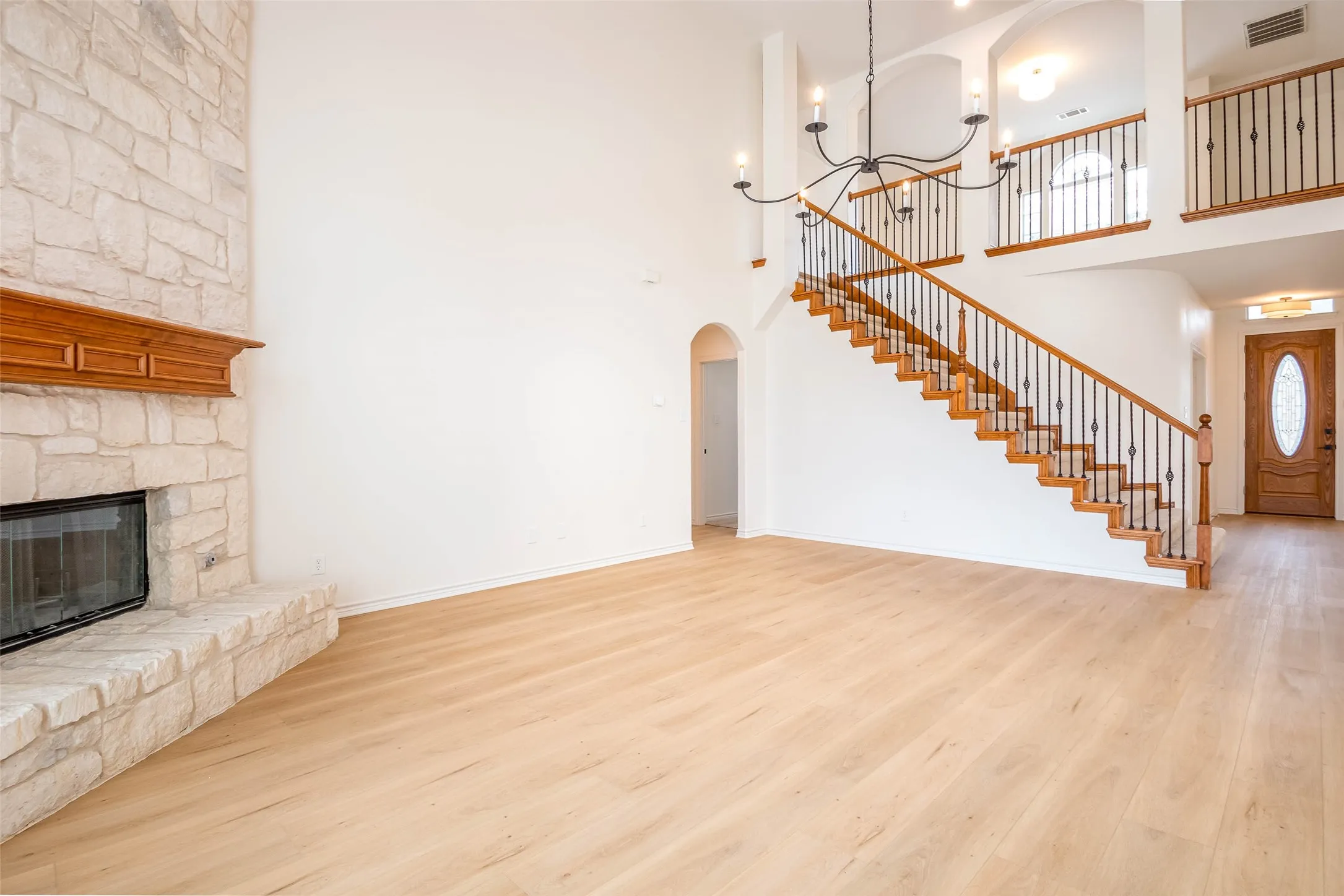 Unfurnished living room featuring wood finished floors, a chandelier, a fireplace, a towering ceiling, and arched walkways
