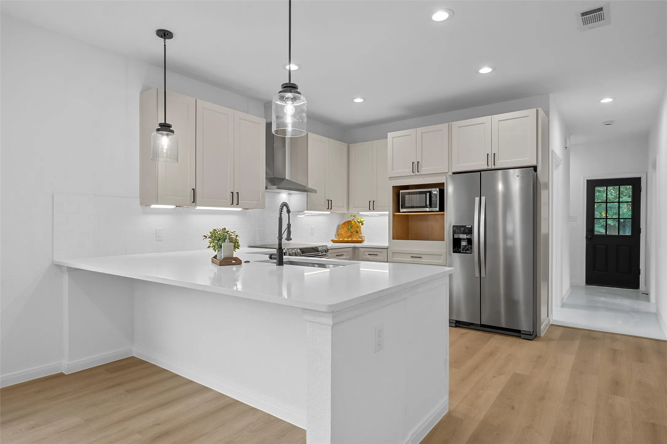 Kitchen featuring appliances with stainless steel finishes, decorative backsplash, light wood-style floors, decorative light fixtures, and a large breakfast area