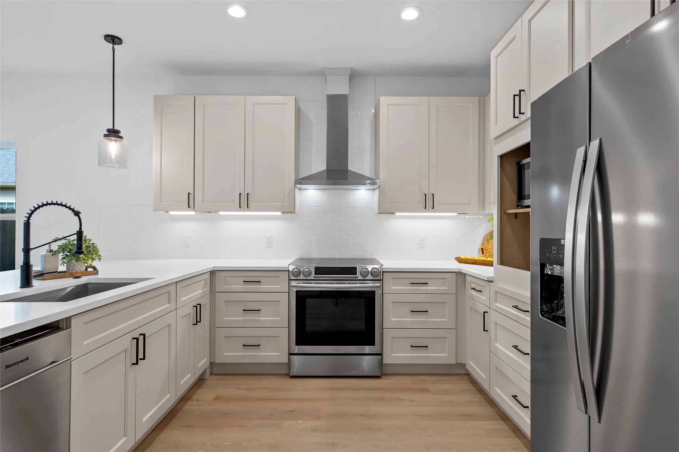Kitchen with appliances with stainless steel finishes, decorative light fixtures, decorative backsplash, light wood finished floors, and range hood